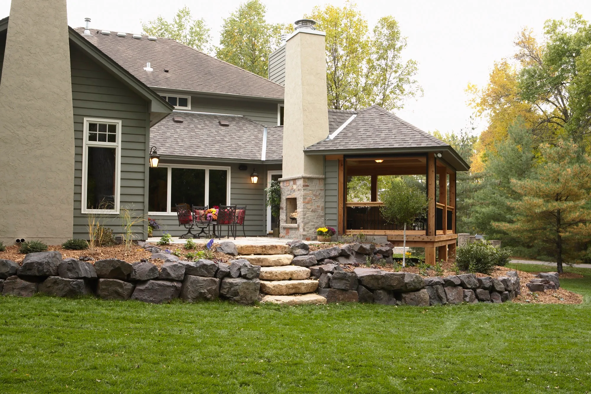 Rear exterior with covered porch, outdoor fireplace, and terraced stone landscape.